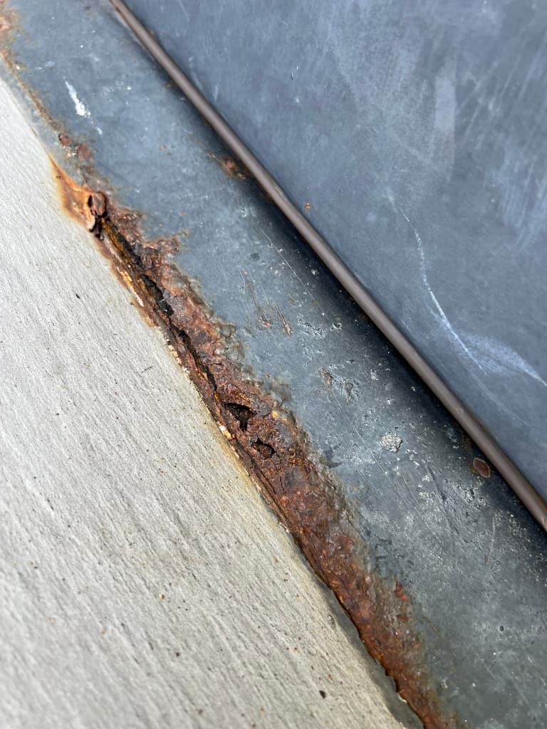 Close-up of a steel door frame jamb rusted and flaking at the floor line