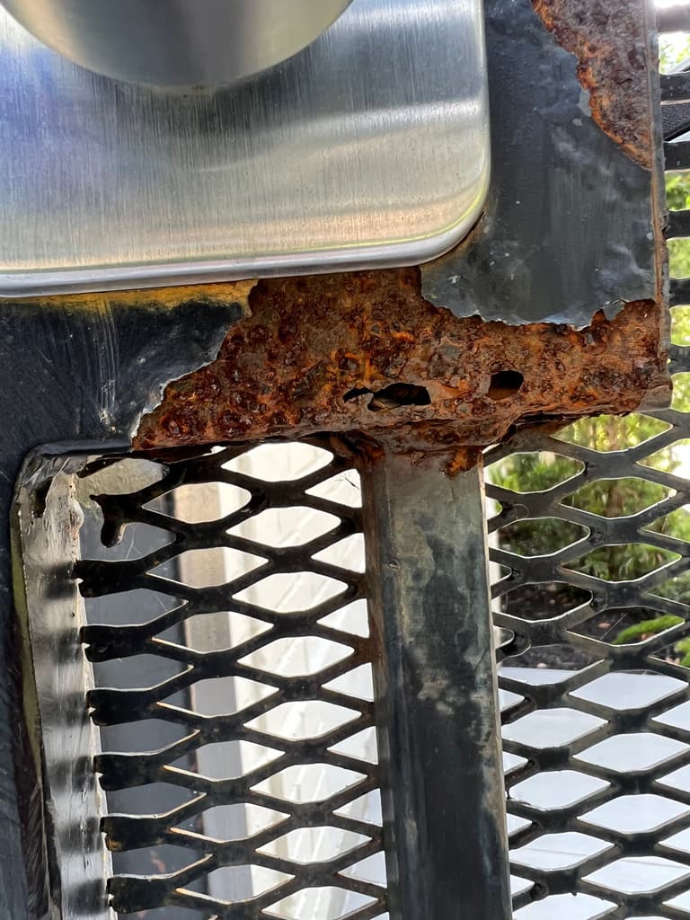 Close-up of a gate lock box with the bottom rusted away into holes and flaking scale