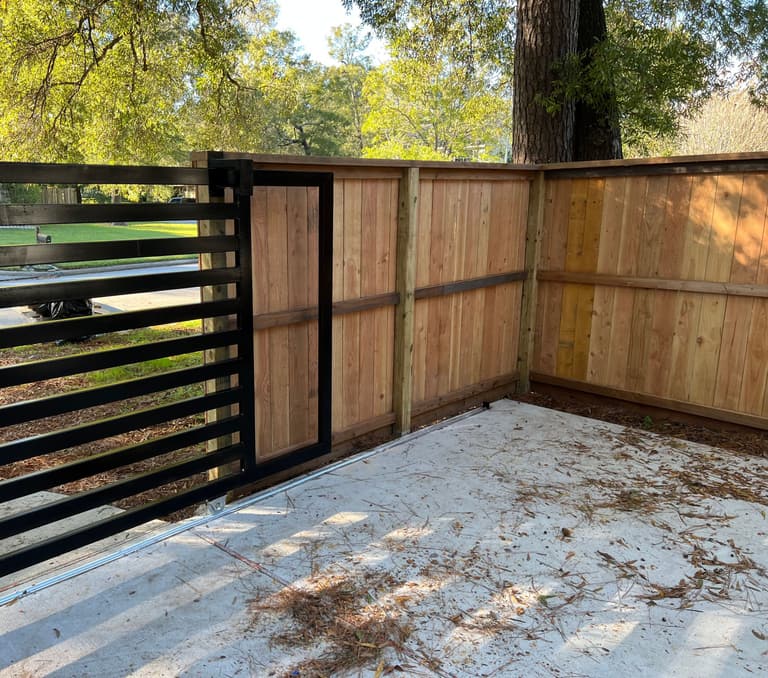 Custom black slat sliding gate closing against a new cedar privacy fence